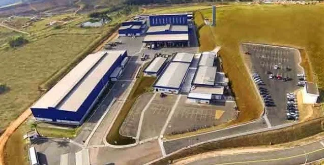 Vista aérea de complexo industrial com galpões de cobertura azul, docas de carga e estacionamento
